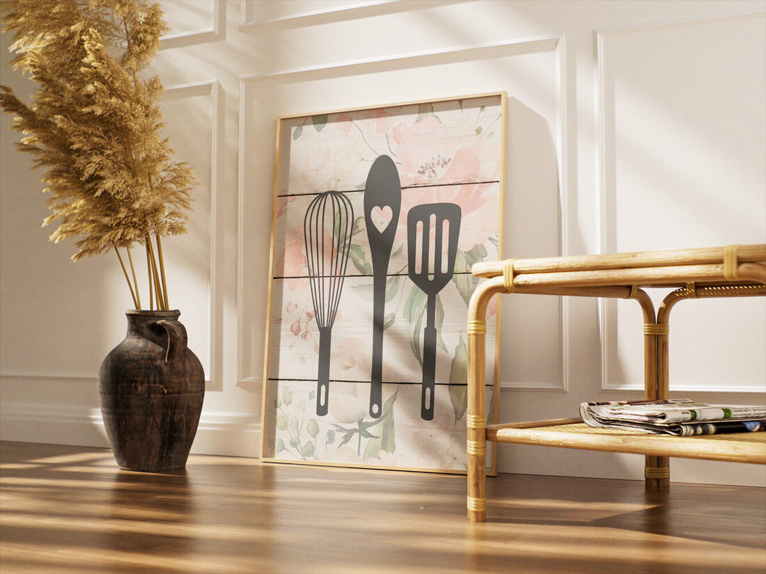 Dark gray silhouettes of a whisk, a wooden spoon with a heart cutout, and a slotted spatula on a floral wood background.